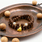 Brown beaded bracelet with a yellow charm on a copper tray