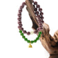 Two-cycle Aromatherapy beaded bracelets, one purple and one green with a gold charm, on a wooden branch.