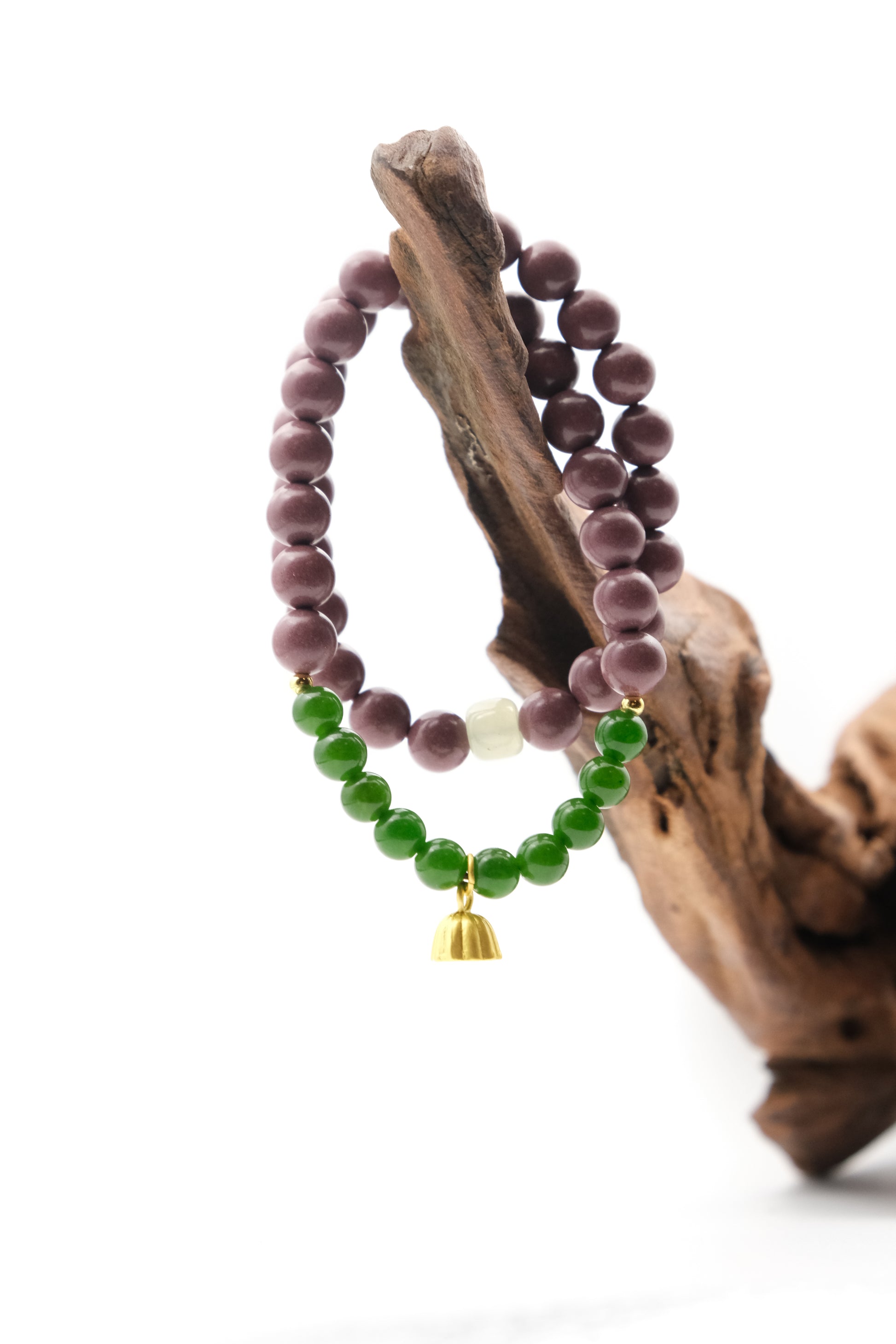 Two-cycle Aromatherapy beaded bracelets, one purple and one green with a gold charm, on a wooden branch.