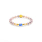 A Tibetan Five Elements Flow Bracelet featuring soft - pink beads interspersed with golden accents. A prominent blue agate bead is centered among them, flanked by unique incense - glass beads. A golden plum blossom charm adds an elegant touch. This bracelet is believed to aid in emotional healing, attract wealth, and offer spiritual protection. 
