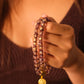 Hand holding Tibetan Five Elements Flow Bracelet with Purple Foil Ash-Glass & Temple Charm for Clarity, Calm & Spiritual Insightagainst a blurred background