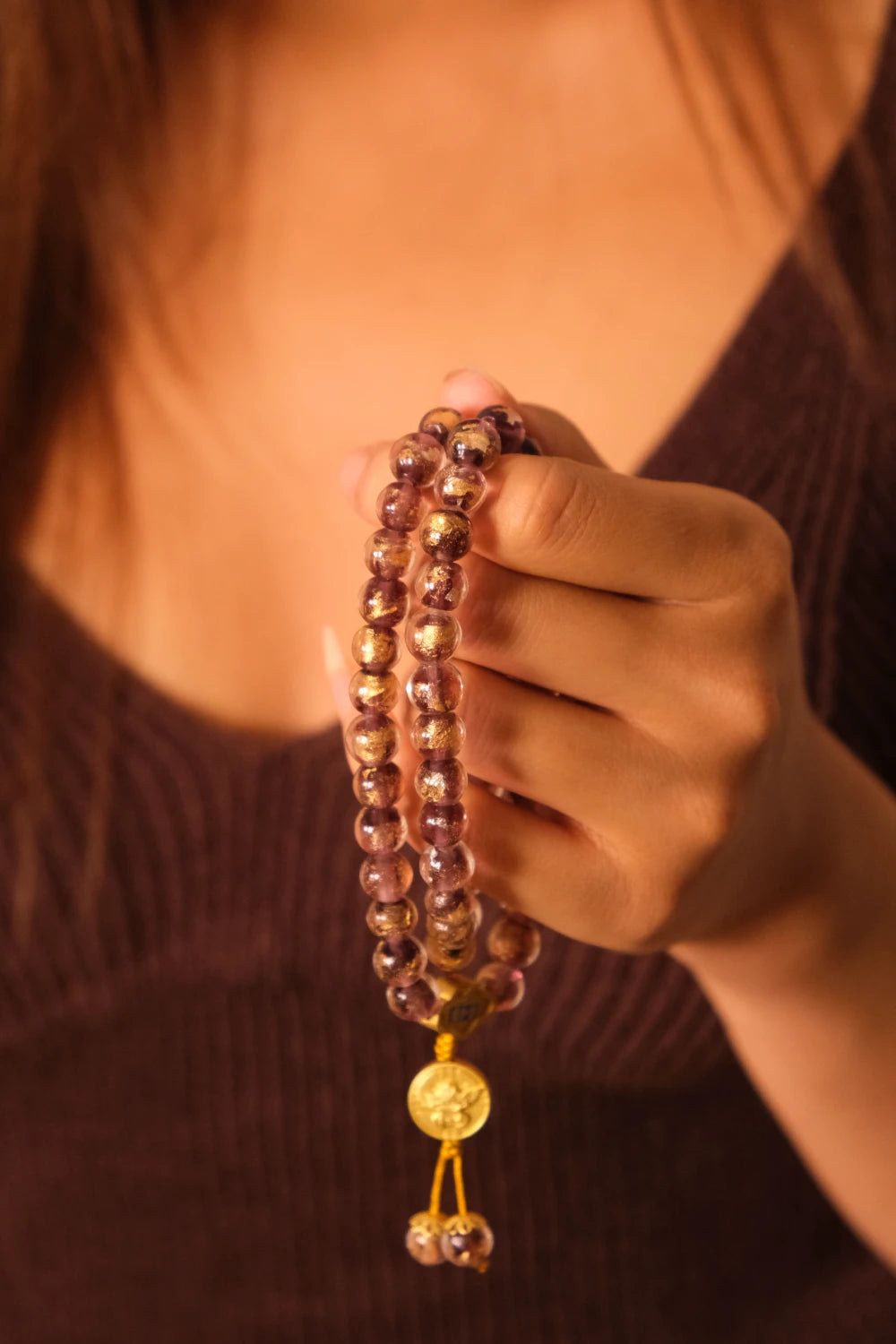 Hand holding Tibetan Five Elements Flow Bracelet with Purple Foil Ash-Glass & Temple Charm for Clarity, Calm & Spiritual Insightagainst a blurred background