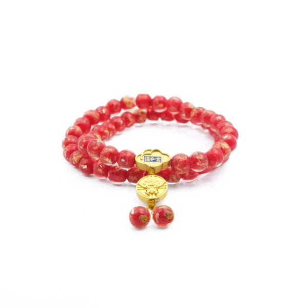 A double - stranded Tibetan Five Elements Flow Bracelet crafted with vibrant red foil ash - glass beads. It features a golden temple charm, adorned with a small decorative piece that has blue inlays. Hanging from the charm are two red beads. This bracelet is thought to promote vitality, attract abundance, and offer spiritual protection. 