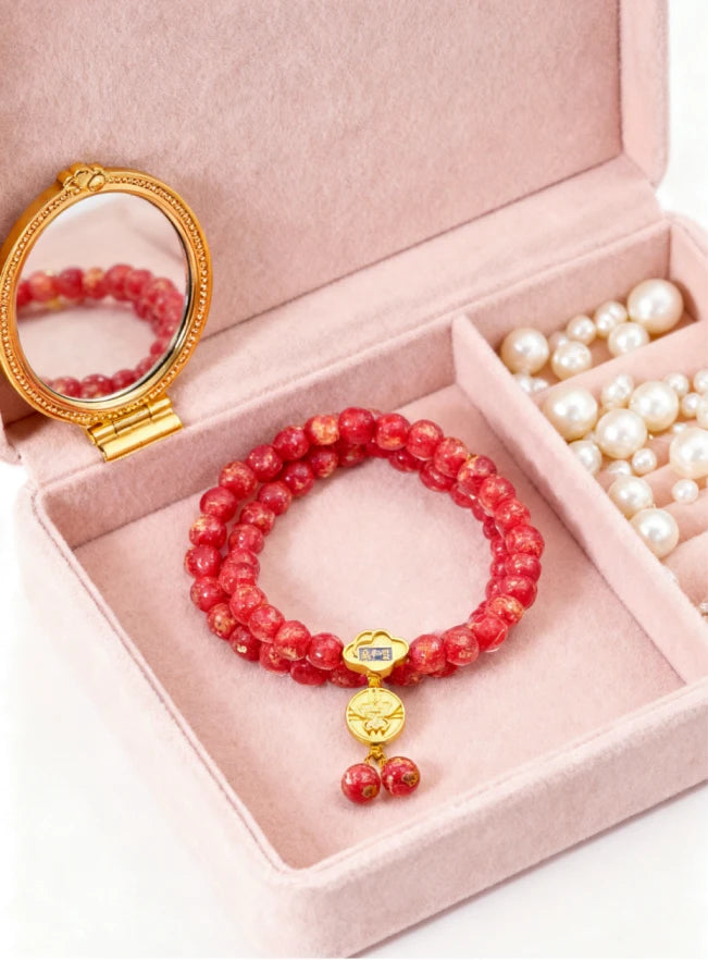Red beaded bracelet with a gold charm in an open jewelry box with a mirror.
