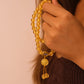 Hand holding a Tibetan Five Elements Flow Bracelet with Yellow Foil Ash-Glass & Temple Charm for Clarity, Prosperity & Grounded Wisdom against a neutral background