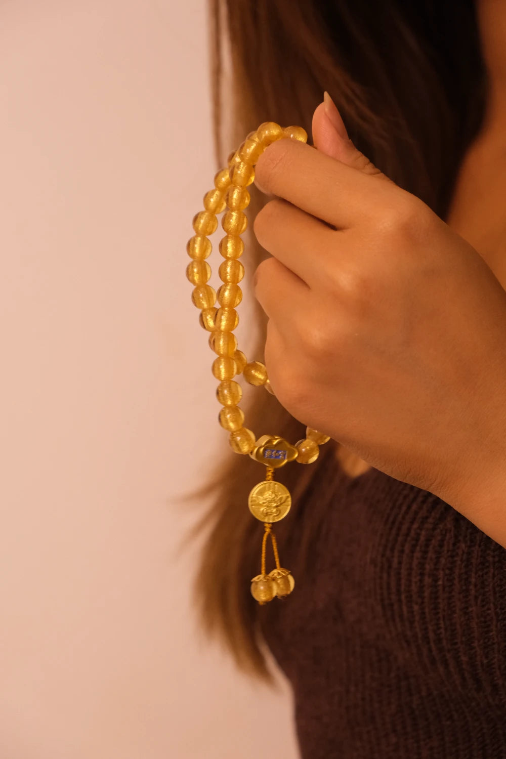 Hand holding a Tibetan Five Elements Flow Bracelet with Yellow Foil Ash-Glass & Temple Charm for Clarity, Prosperity & Grounded Wisdom against a neutral background