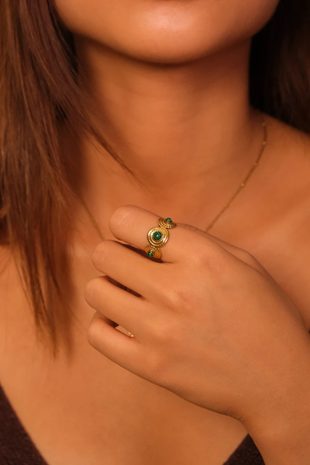 Close-up of a hand wearing a gold ring with malachite stone on a blurred background