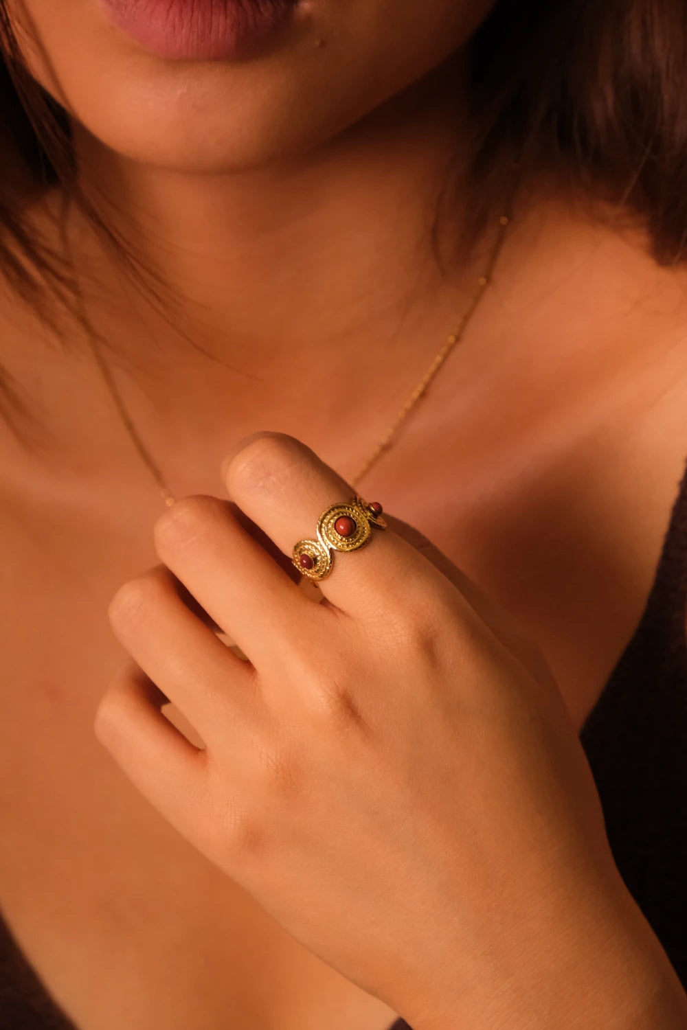 Close-up of a hand wearing a gold ring with a Red Agate gemstone against a blurred background