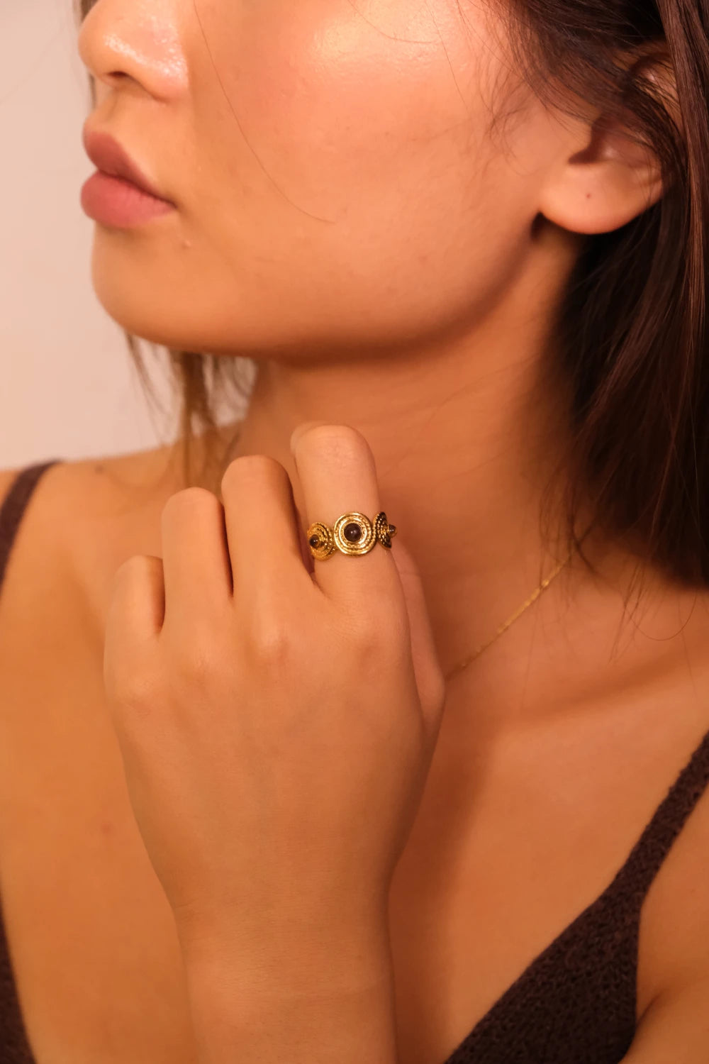 Close-up of a woman's hand wearing a Tibetan Five Elements Ring with a pink background. Tiger’s Eye stone for Success & Abundance