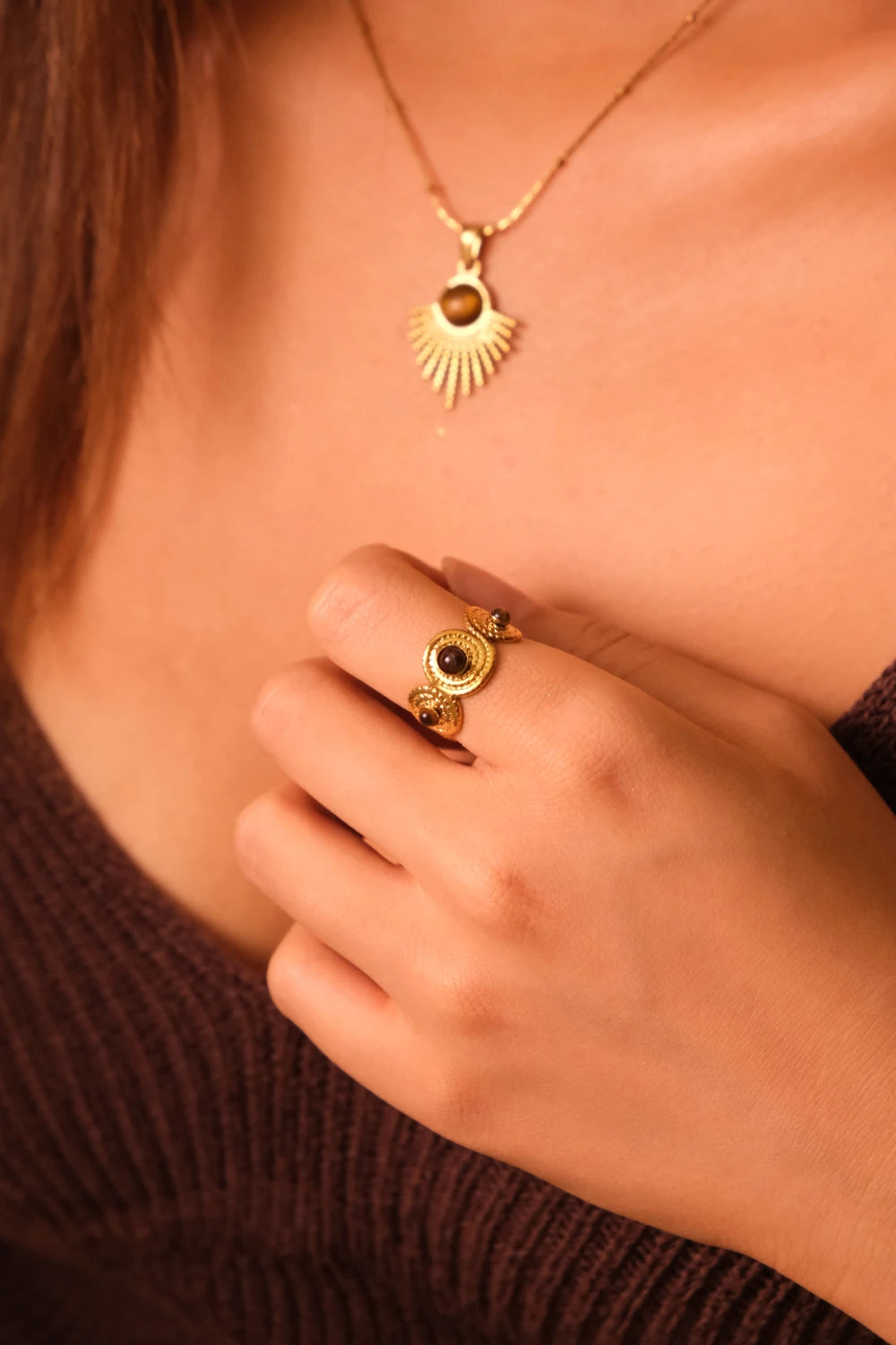 Close-up of a person wearing a gold Tibetan Five Elements Ring – Tiger’s Eye for Success & Abundance ring  and necklace with a sun design.