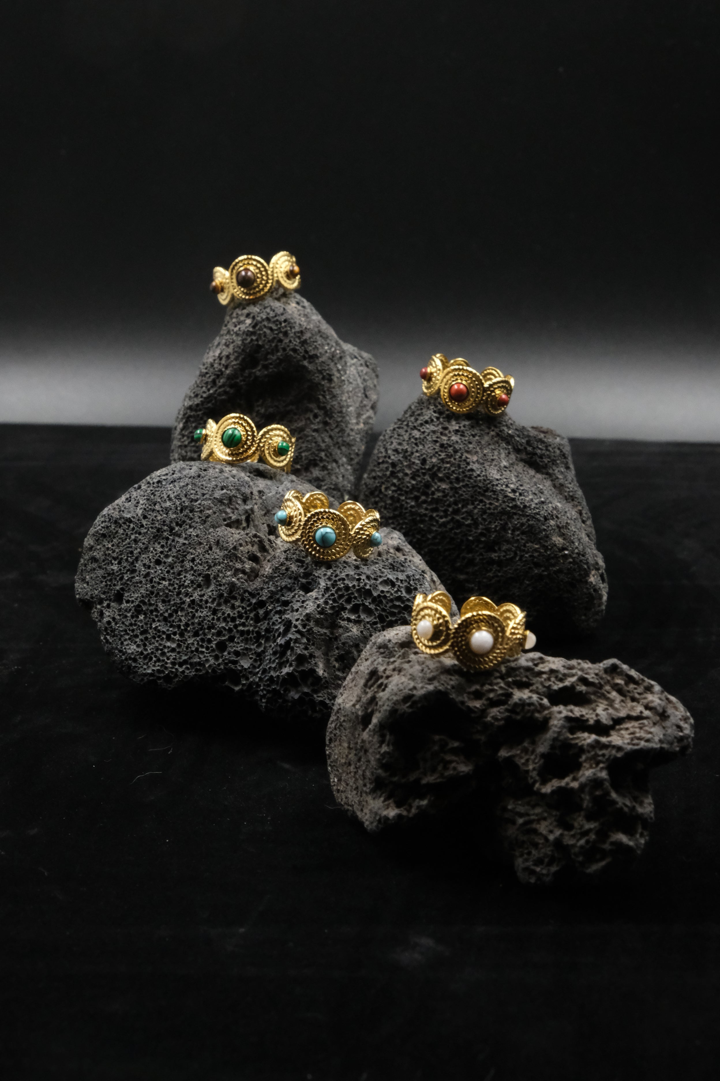Gold earrings with gemstones on a dark textured surface. Tibetan Five Elements Ring