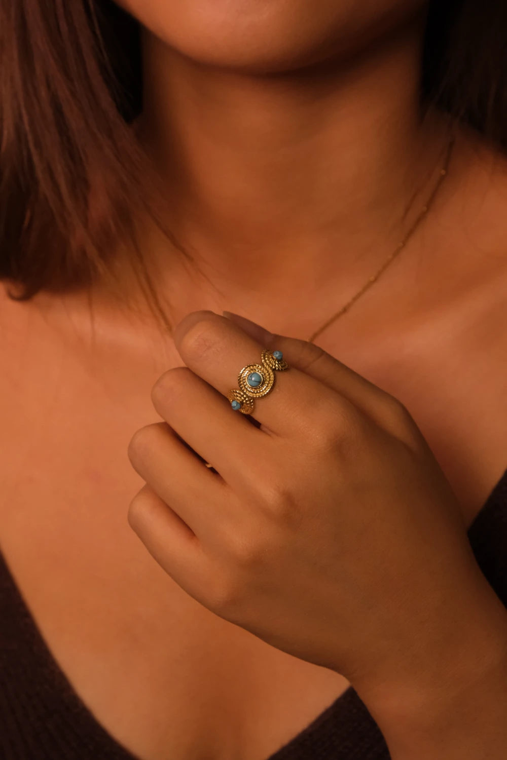 Close-up of a hand wearing a gold ring with a turquoise stone against a blurred background. Tibetan Five Elements Ring