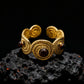 A gold adjustable ring featuring three brown Tiger's Eye stones resting on a black volcanic rock.