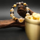 Tibetan Goldwish Crystal Bracelet with multicolored beads on a wooden branch with a gold container in the background.