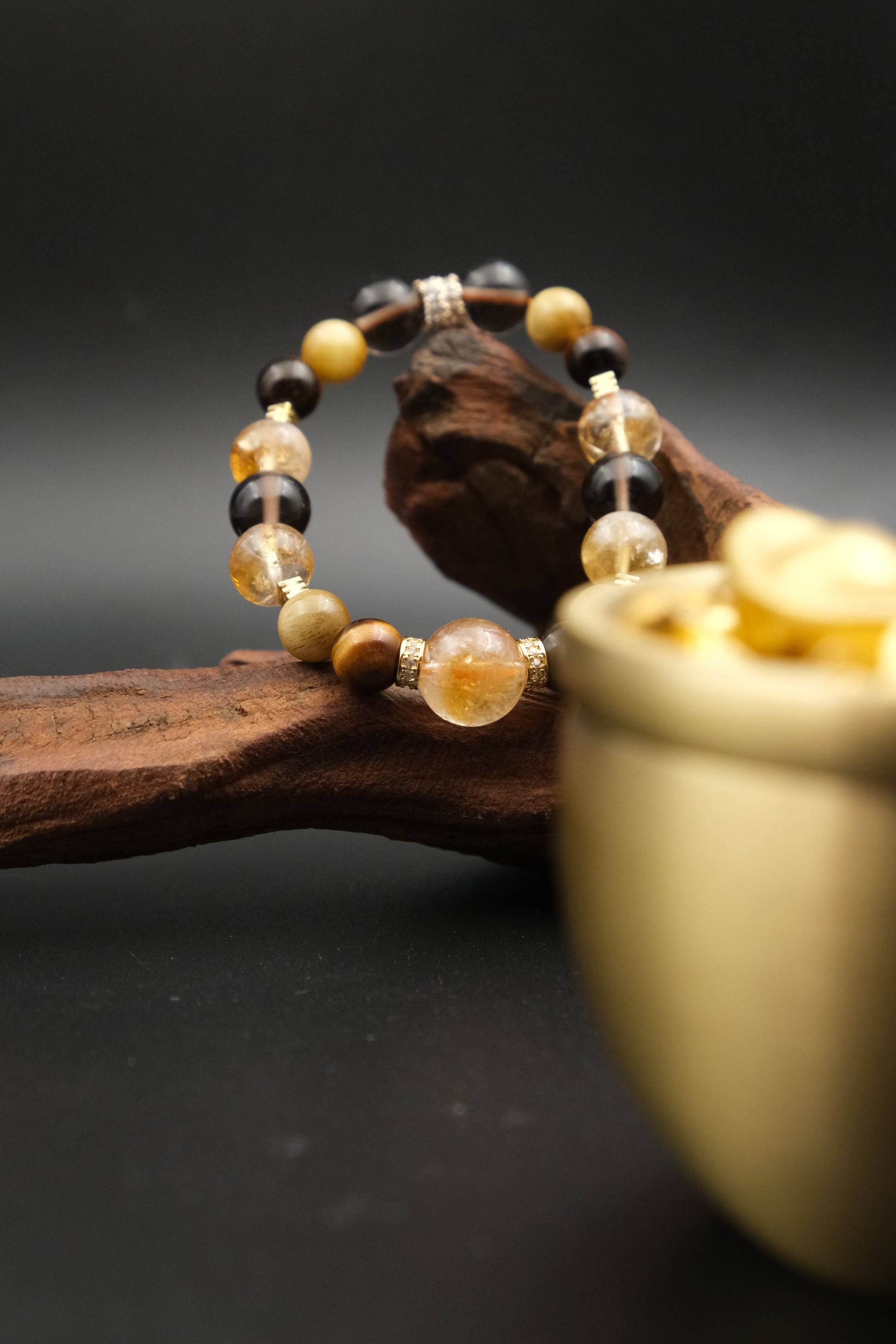 Tibetan Goldwish Crystal Bracelet with multicolored beads on a wooden branch with a gold container in the background.