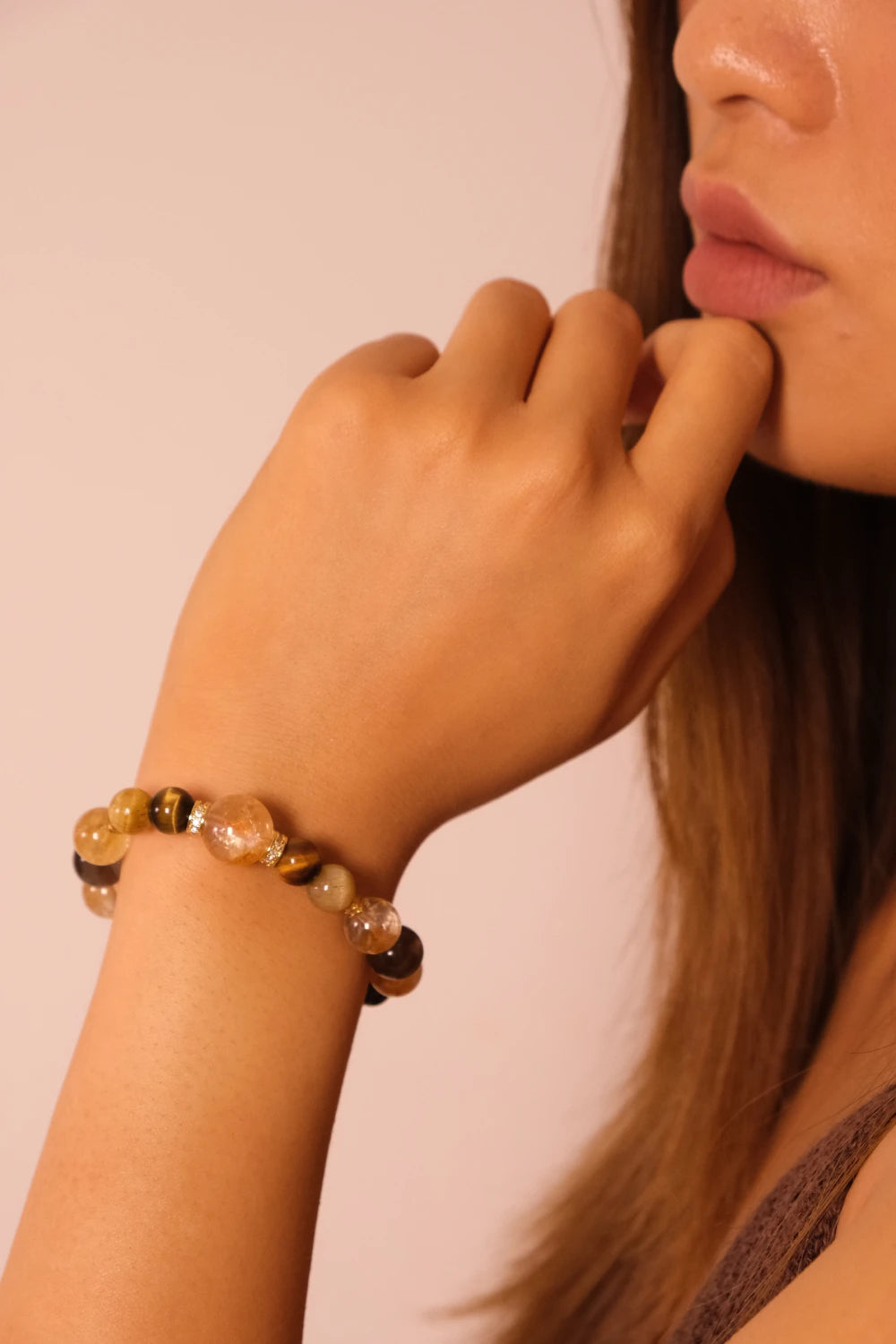 Close-up of a hand wearing a Tibetan Goldwish Crystal Bracelet on a plain background