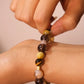 Hand wearing a Tibetan Goldwish Crystal Bracelet - Citrine & Tiger Eye, Symbol of Abundance, Money Magnet & Success with a neutral background