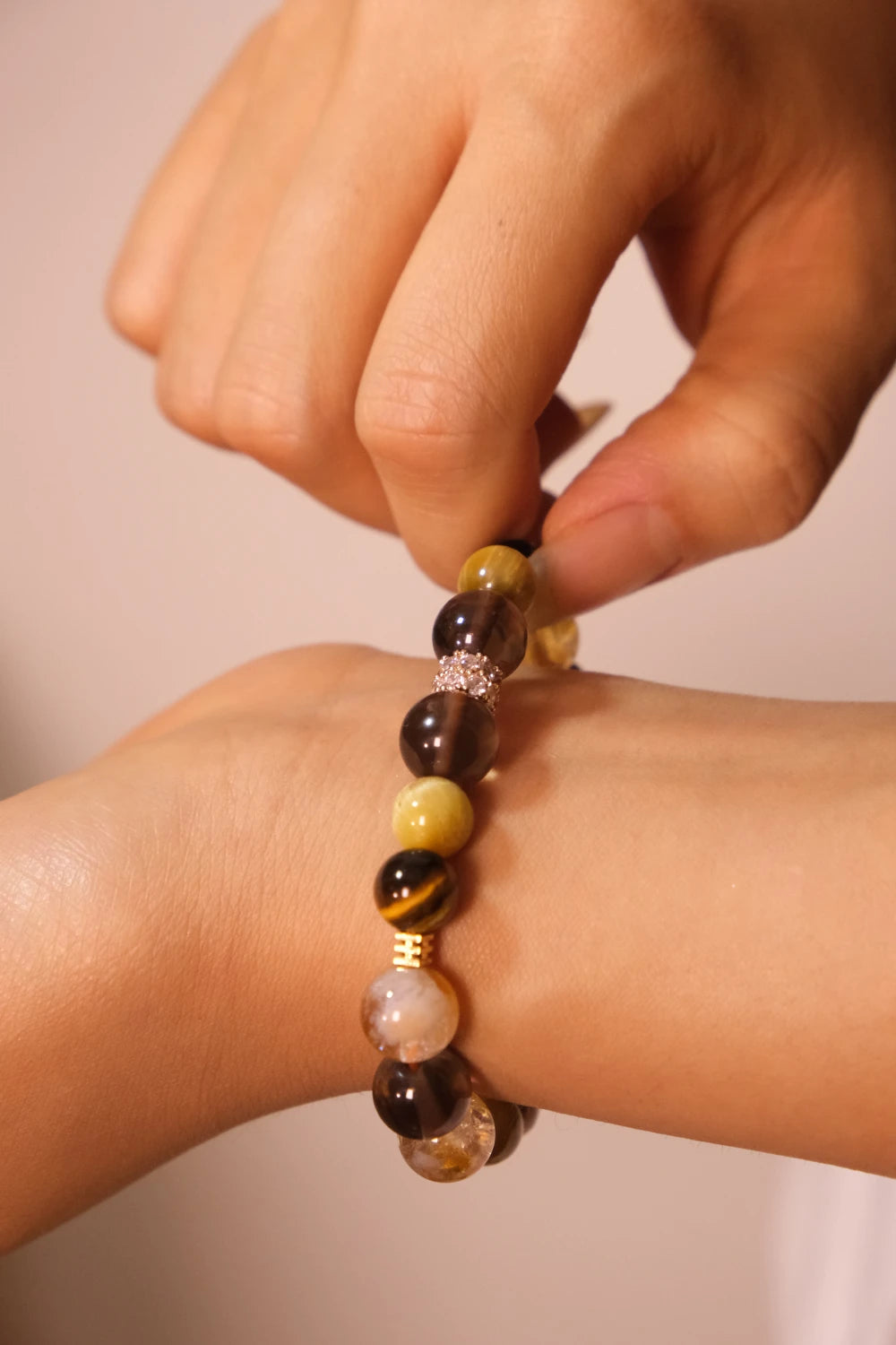 Hand wearing a Tibetan Goldwish Crystal Bracelet - Citrine & Tiger Eye, Symbol of Abundance, Money Magnet & Success with a neutral background