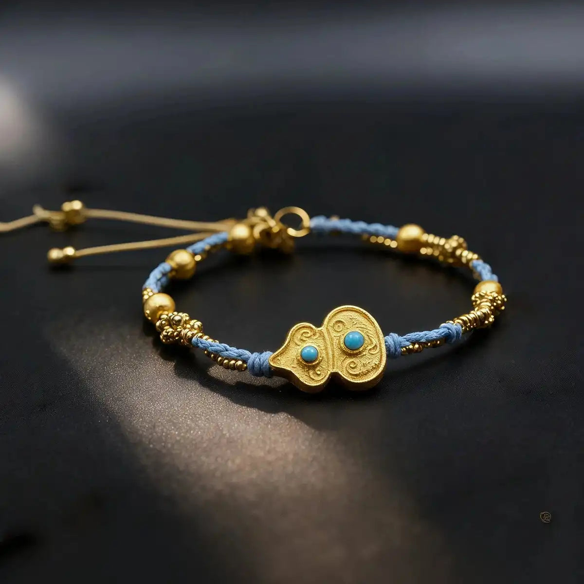 A gold-plated Tibetan Gourd (hulu) bracelet resting on a dark surface. It features light blue woven cord and golden spacer beads, with a central turquoise-inlaid gold gourd charm symbolizing luck, wealth, and warding off evil spirits.