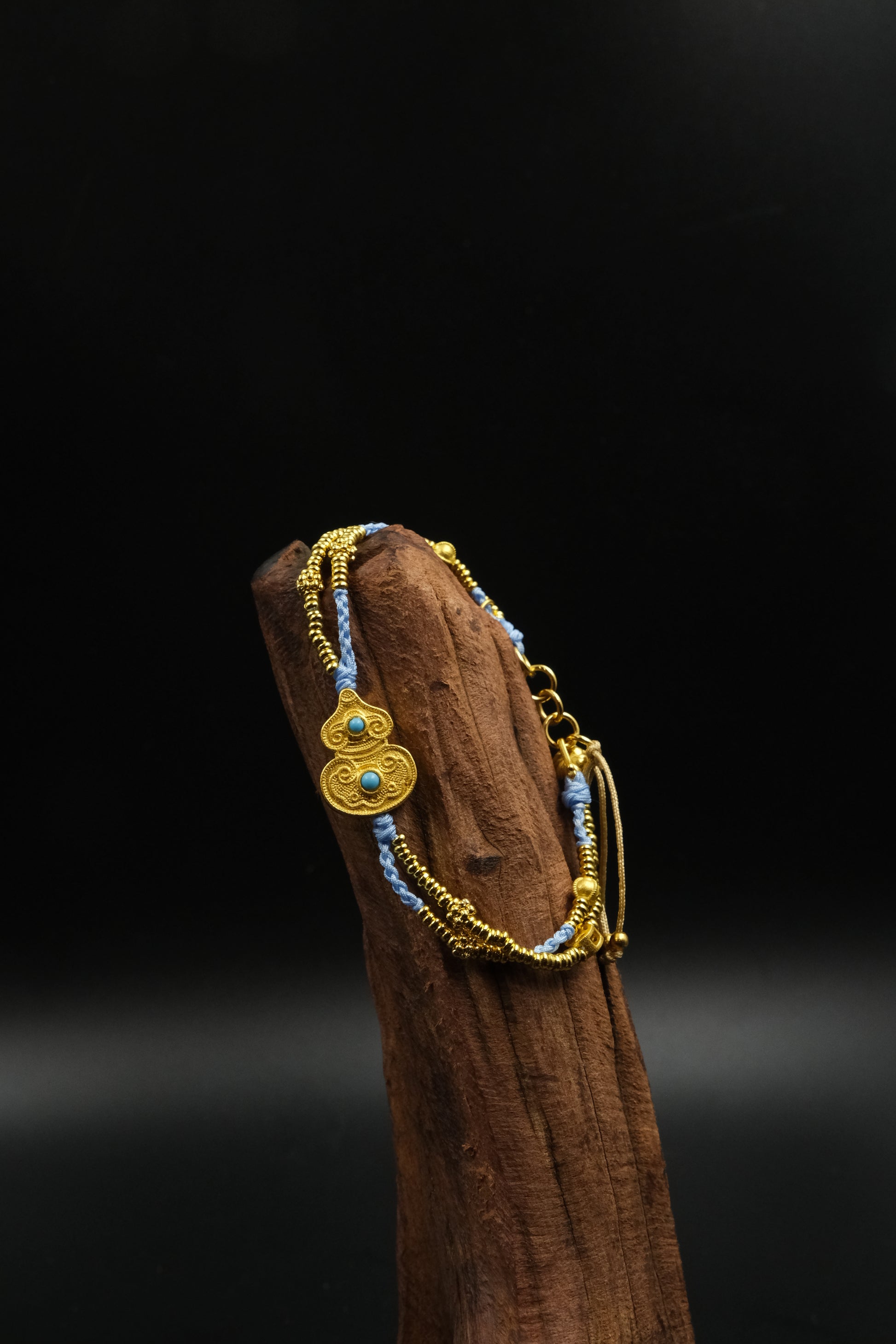 Tibetan Harmony Double Bracelet – Gourd & Turquoise for Luck & Protection on a cinnamon stick against a dark background