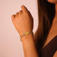 Close-up of a woman's arm wearing a bicolor bracelet on a pink background. Handmade bracelet with gold beads and blue woven cord, featuring a double-circle gold charm with two turquoise.