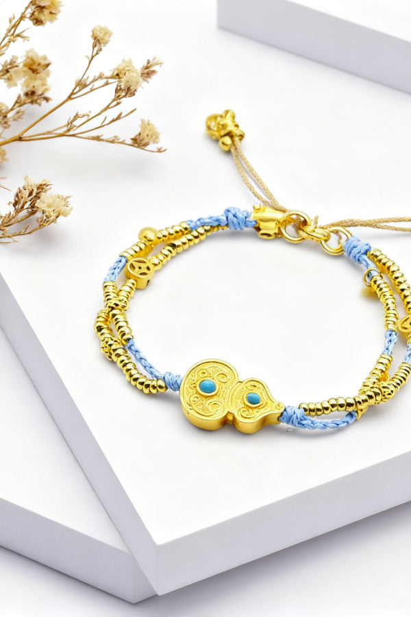 Gold and blue bracelet on a white surface with dried flowers