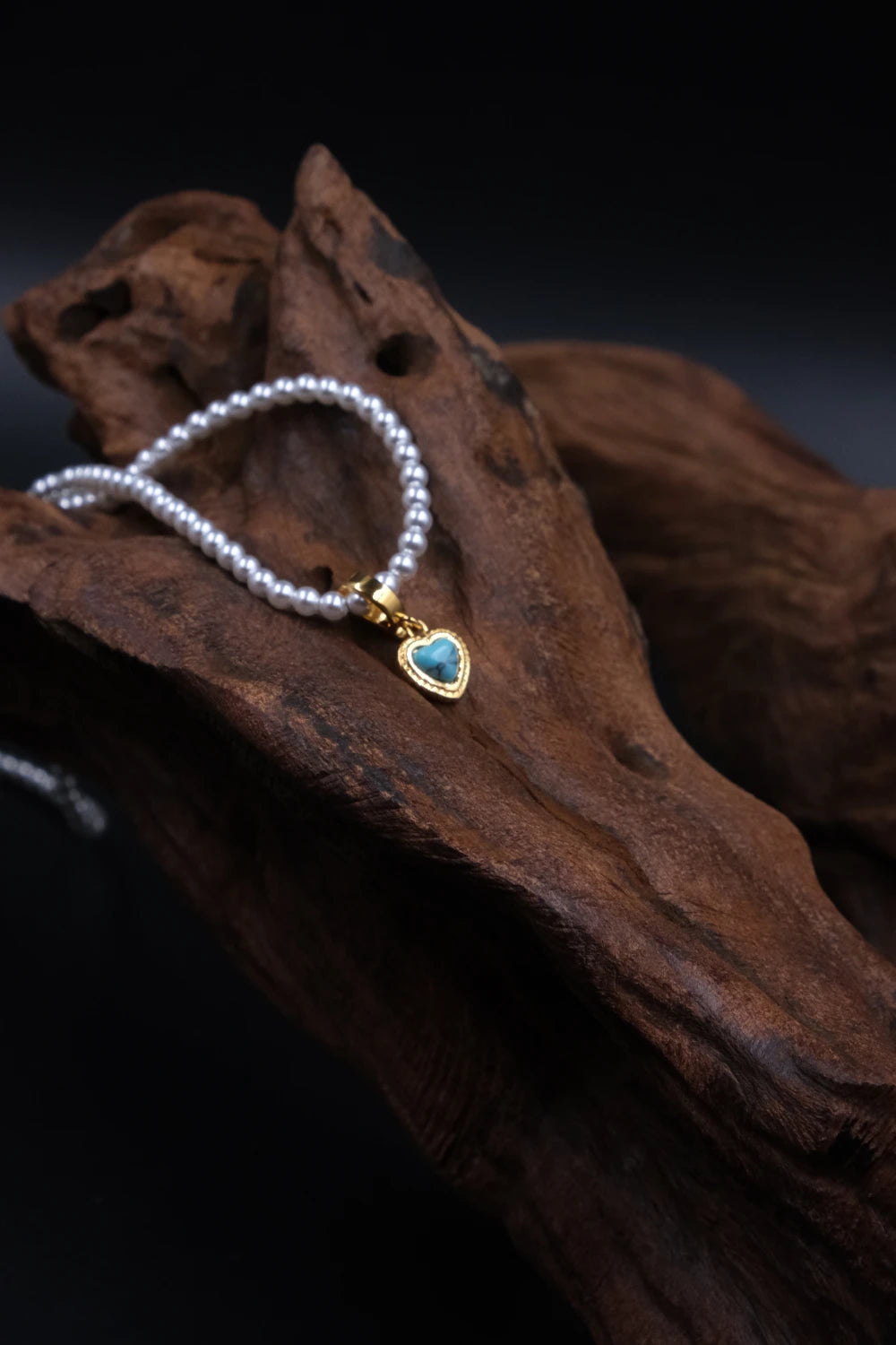 Handcrafted Tibetan Harmony necklace featuring a polished turquoise heart pendant with pearl beads, associated with protection and emotional balance, displayed on wooden surface.