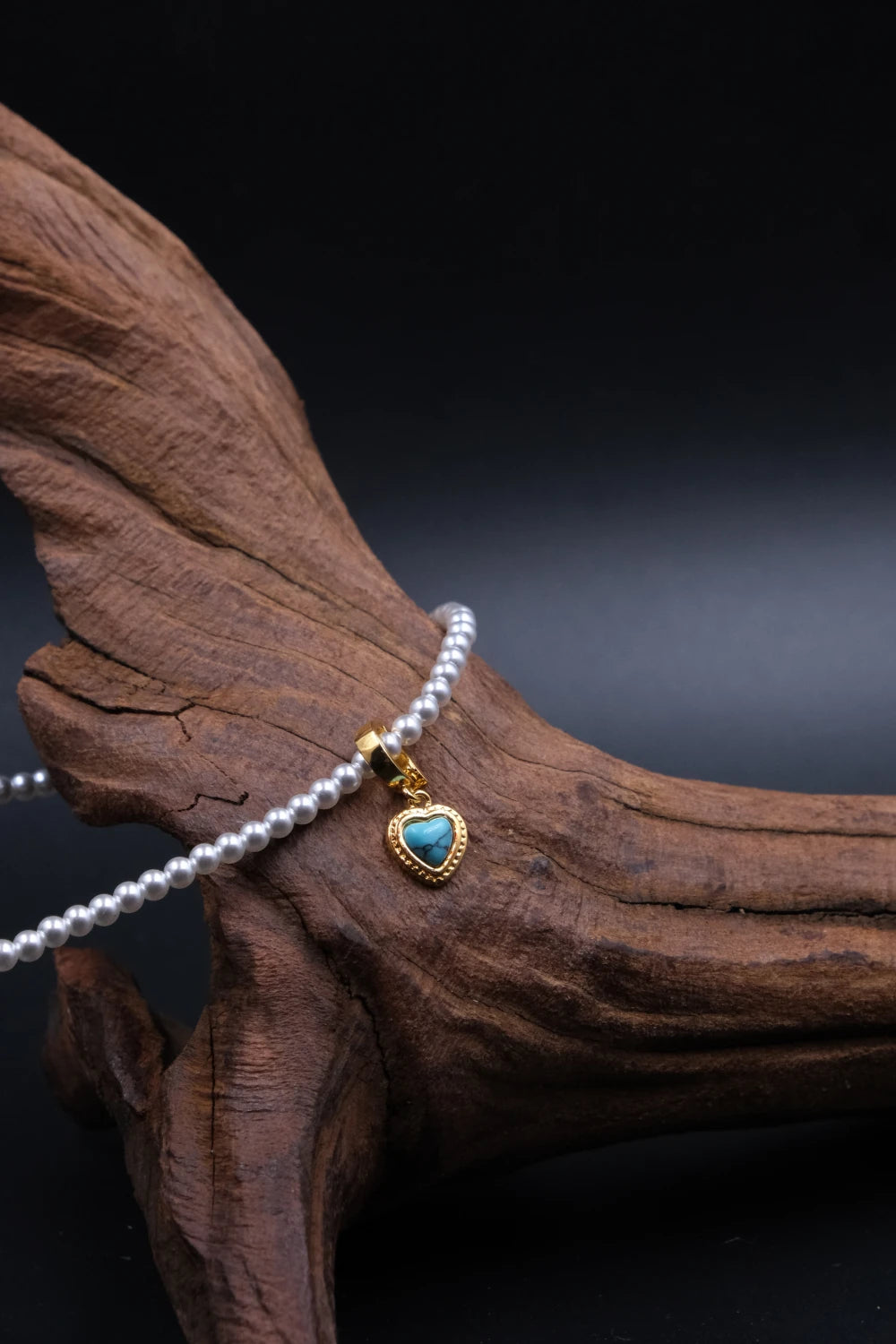Handcrafted Tibetan Harmony necklace featuring a polished turquoise heart pendant with pearl beads, associated with protection and emotional balance, displayed on wooden surface.