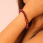 Close-up of a person wearing a purple cinnabar beaded bracelet on a plain background