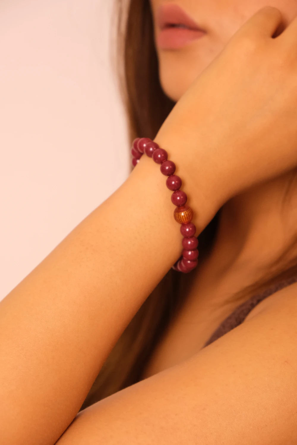 Close-up of a person wearing a purple cinnabar beaded bracelet on a plain background