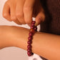 Hand adjusting a Tibetan Heart Sutra Cinnabar beaded bracelet on a wrist against a neutral background
