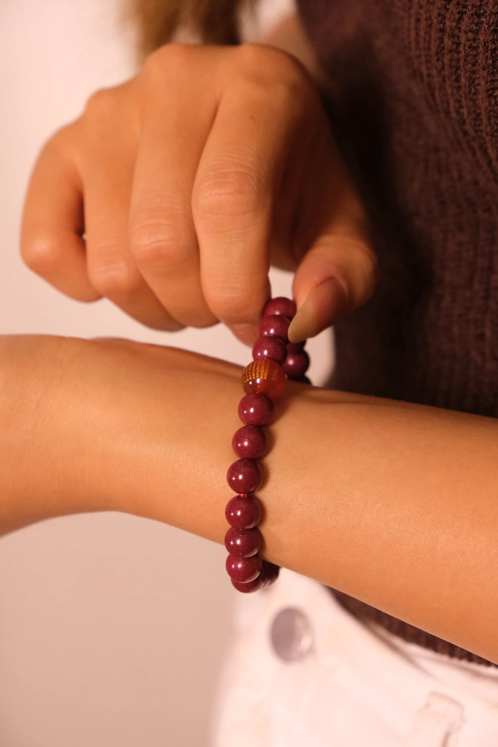 Hand adjusting a Tibetan Heart Sutra Cinnabar beaded bracelet on a wrist against a neutral background