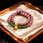 A bracelet with purple and green beads resting on a beige silk cloth in a wooden tray.