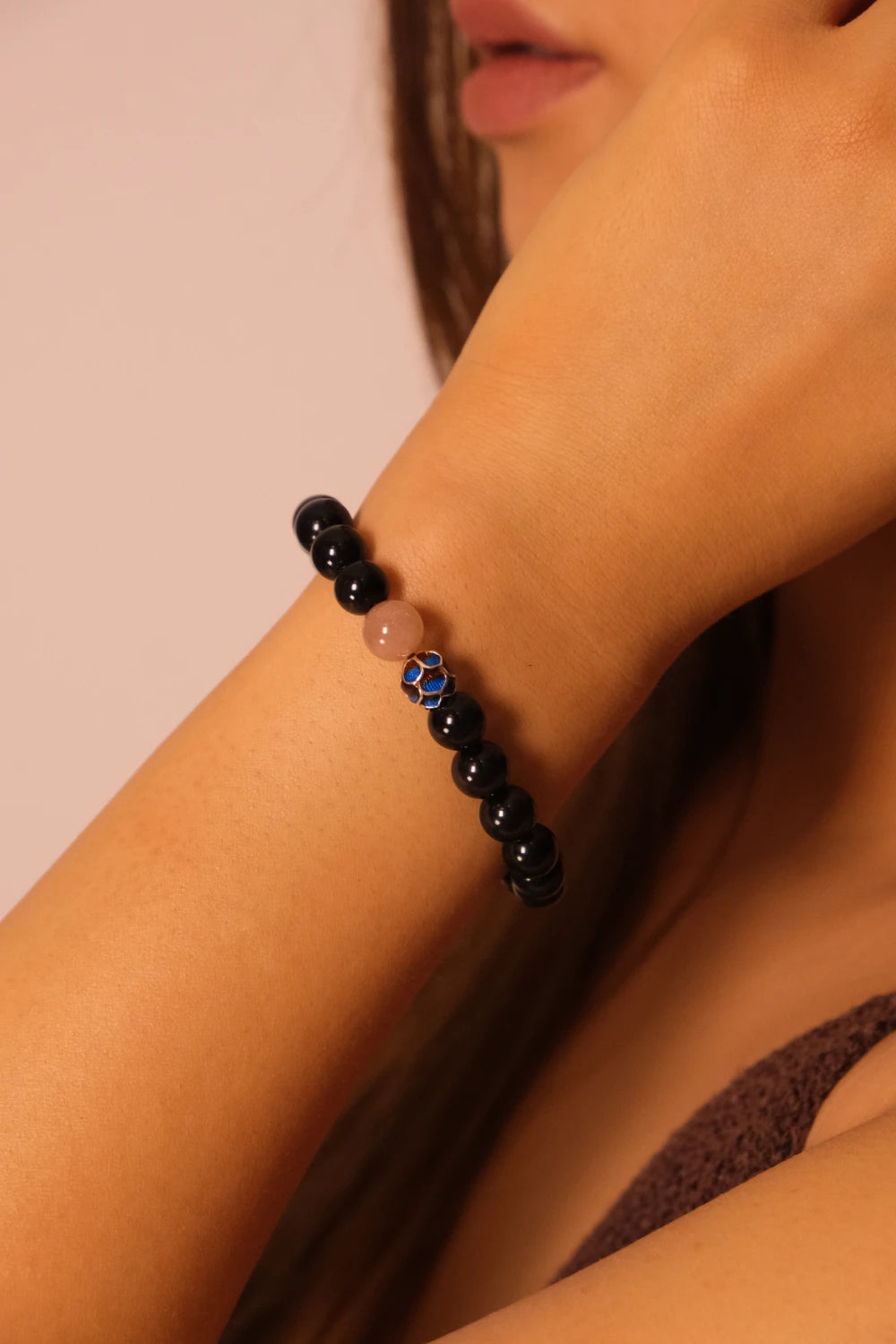Close-up of a person's arm wearing a black beaded bracelet, Protection Vitality Inner Peace, with a pink background