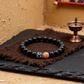 Black beaded bracelet with a blue and gold clasp on a brown fabric with a small bronze container in the background.