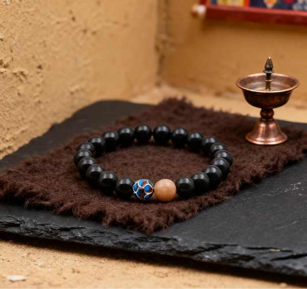 Black beaded bracelet with a blue and gold clasp on a brown fabric with a small bronze container in the background.