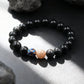A black bead bracelet with one pink stone and one blue enamel bead resting on a black rock.