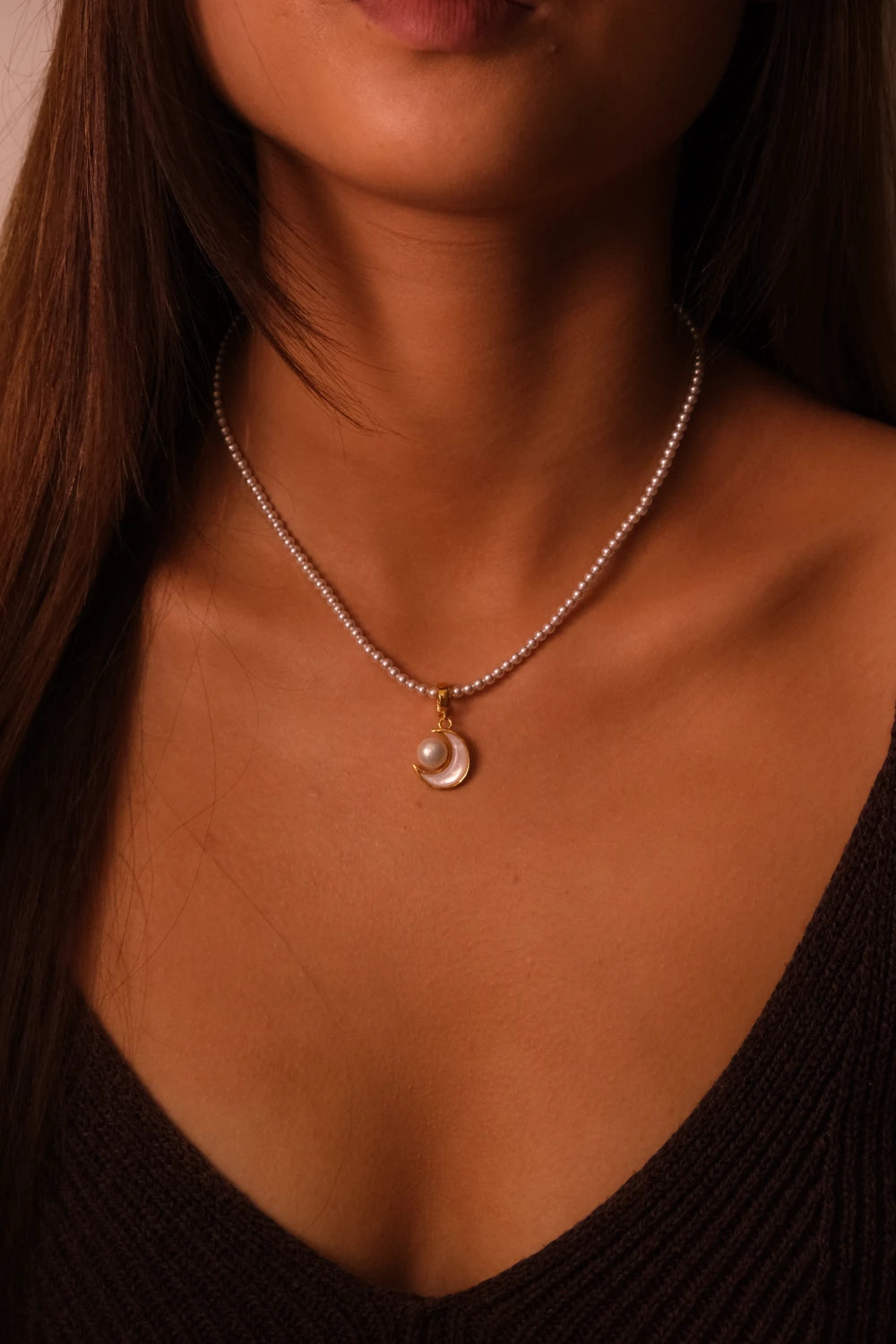 Close-up of a necklace with a pendant on a person wearing a black top.