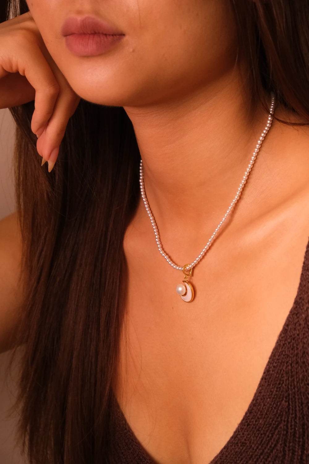 Close-up of a woman wearing a pearl necklace with a moon pendant.