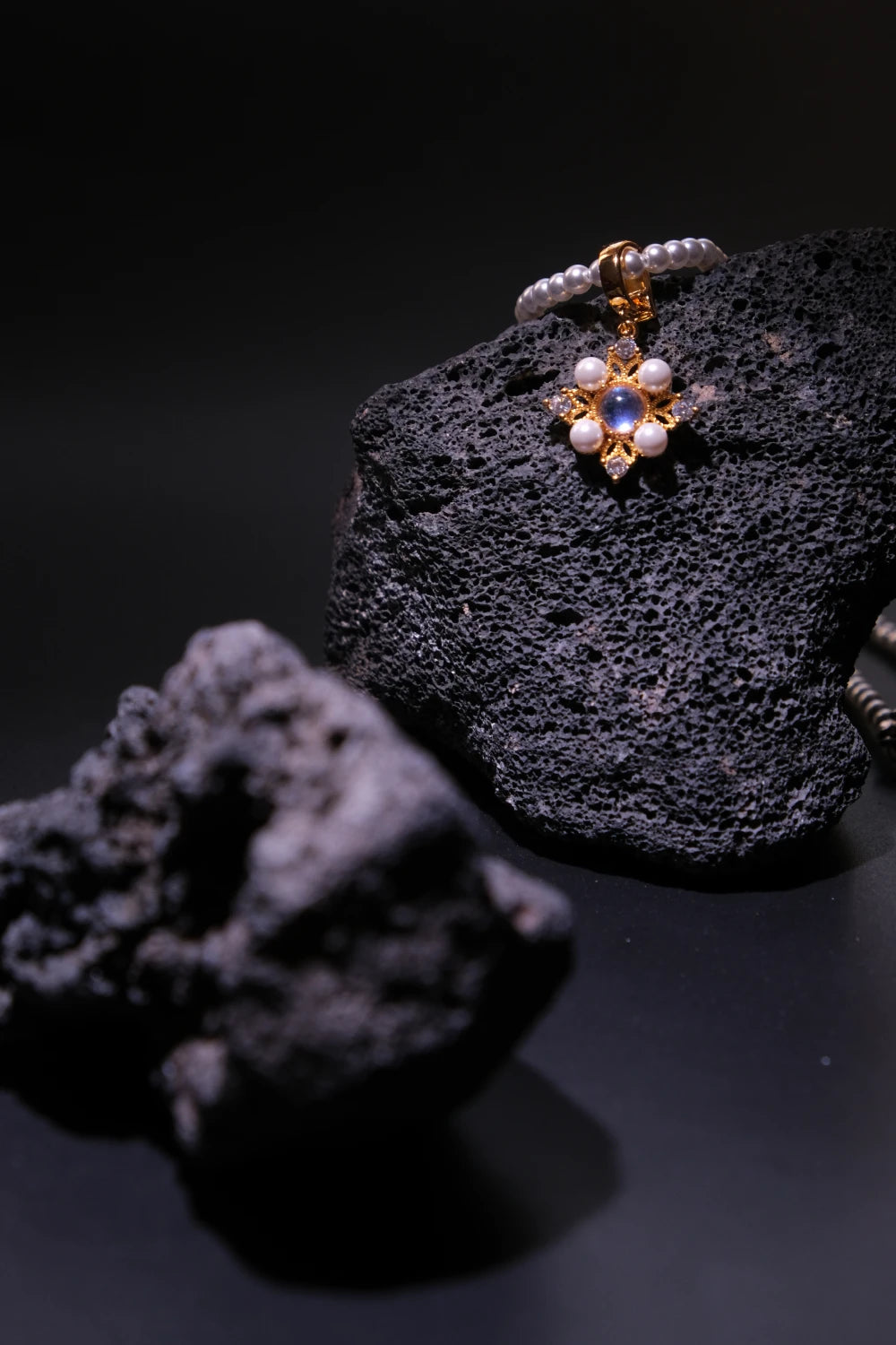 Handcrafted Tibetan Moonstone Pendant Necklace featuring a glowing natural moonstone surrounded by pearls, displayed on volcanic rock, associated with inner calm and emotional harmony.