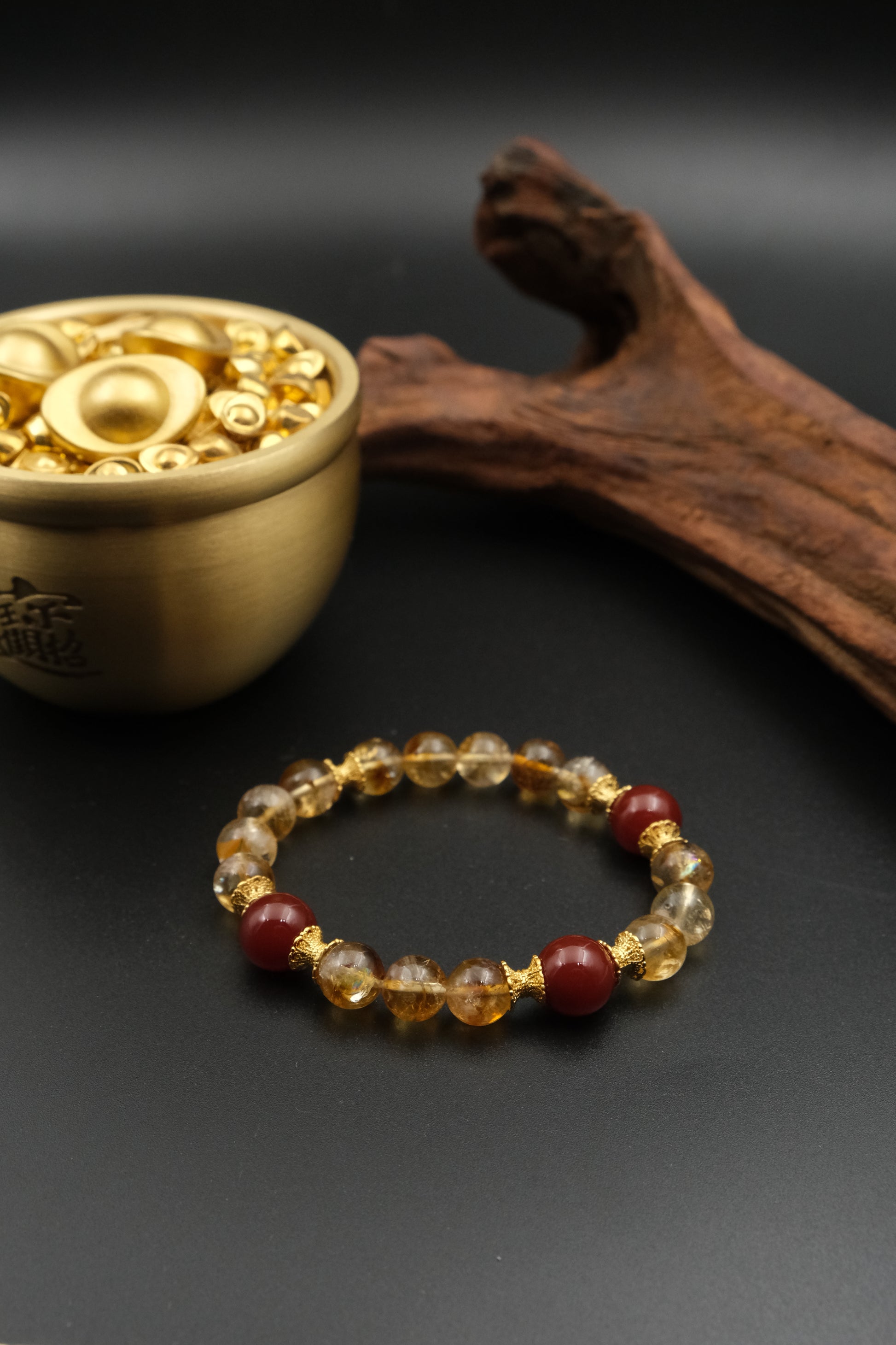 Tibetan Prosperity Energy Bracelet with amber and red beads next to a small brass container on a dark surface