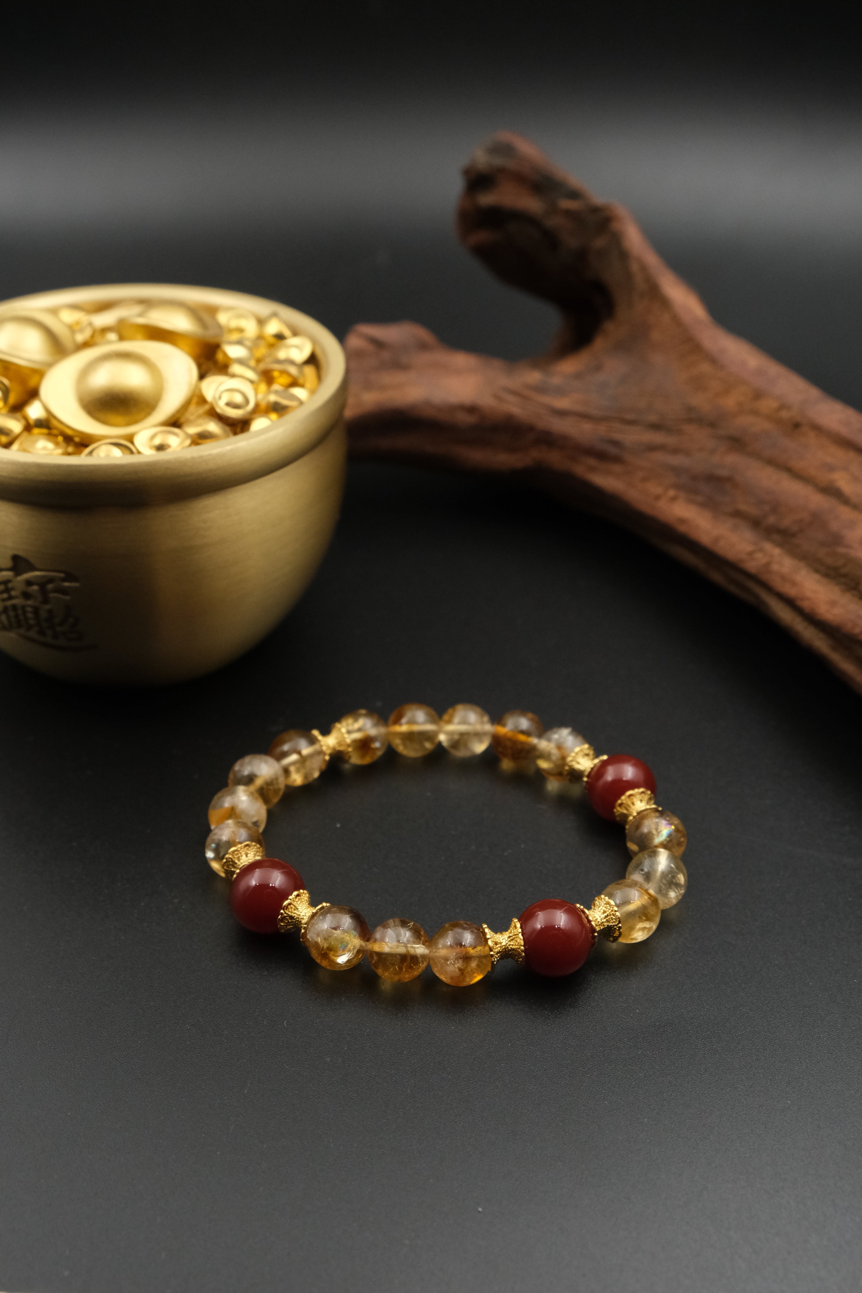 Tibetan Prosperity Energy Bracelet with amber and red beads next to a small brass container on a dark surface