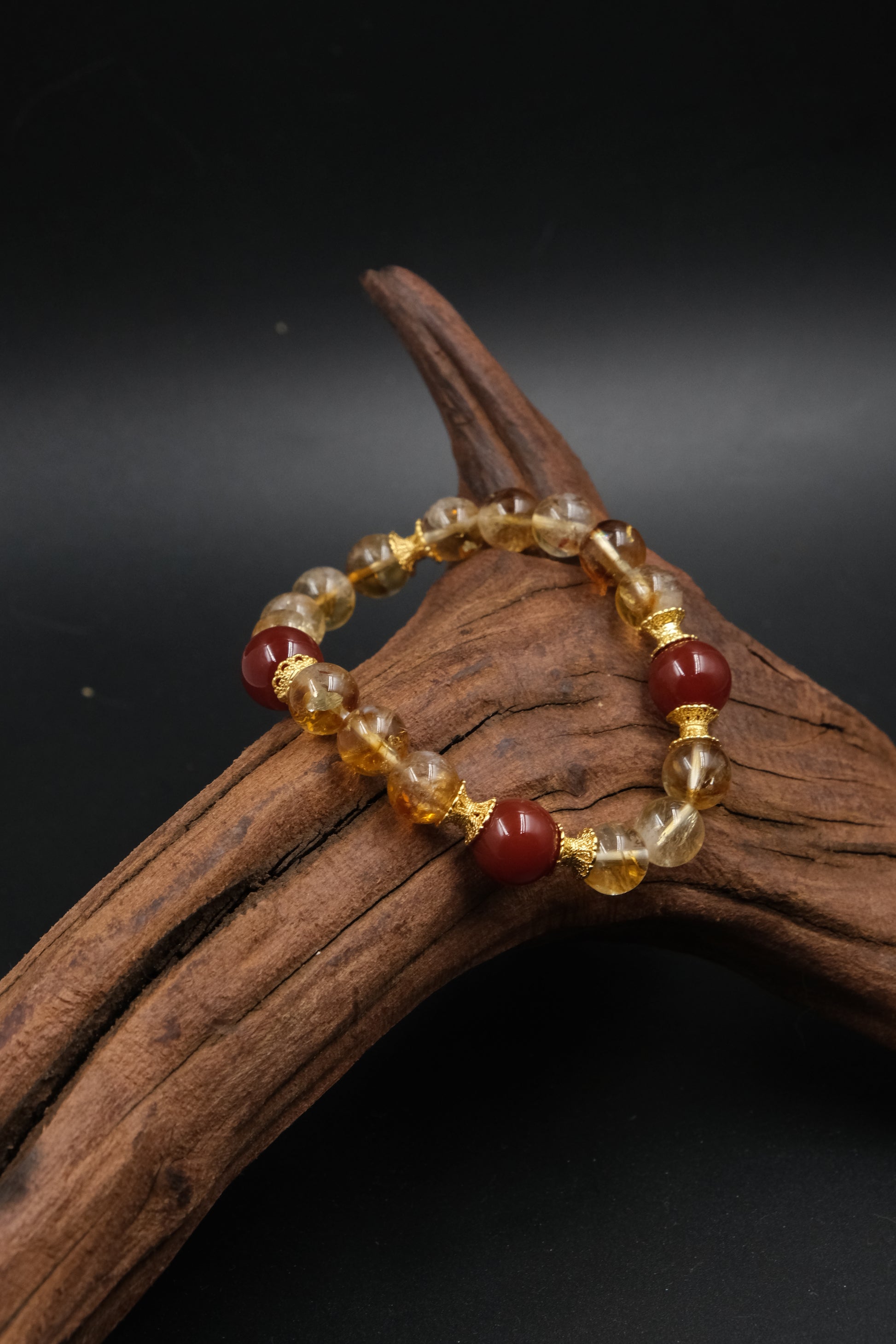 Tibetan Prosperity Energy Beaded bracelet with red and gold beads on a wooden branch against a dark background