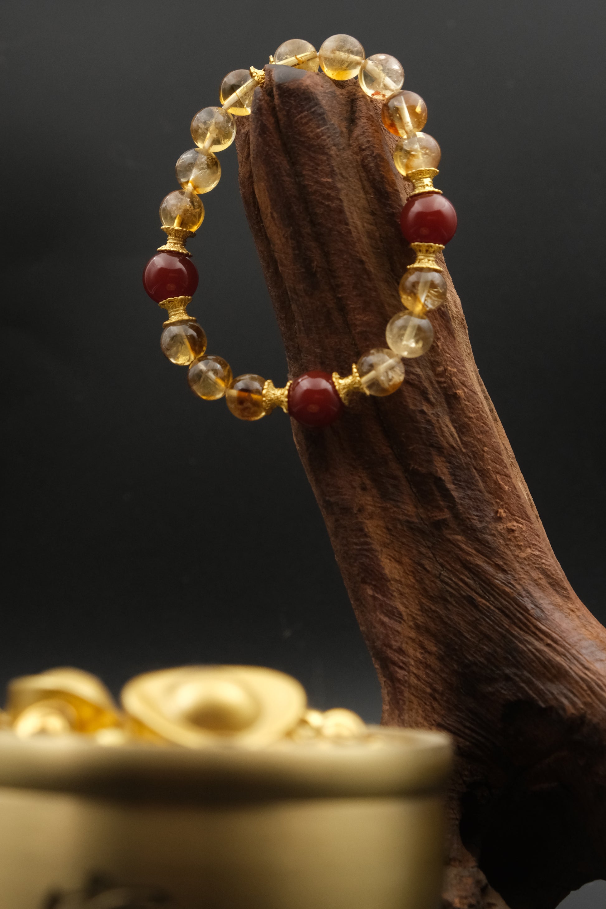 Tibetan Prosperity EnergyBeaded bracelet with red and gold beads on a wooden stick against a dark background