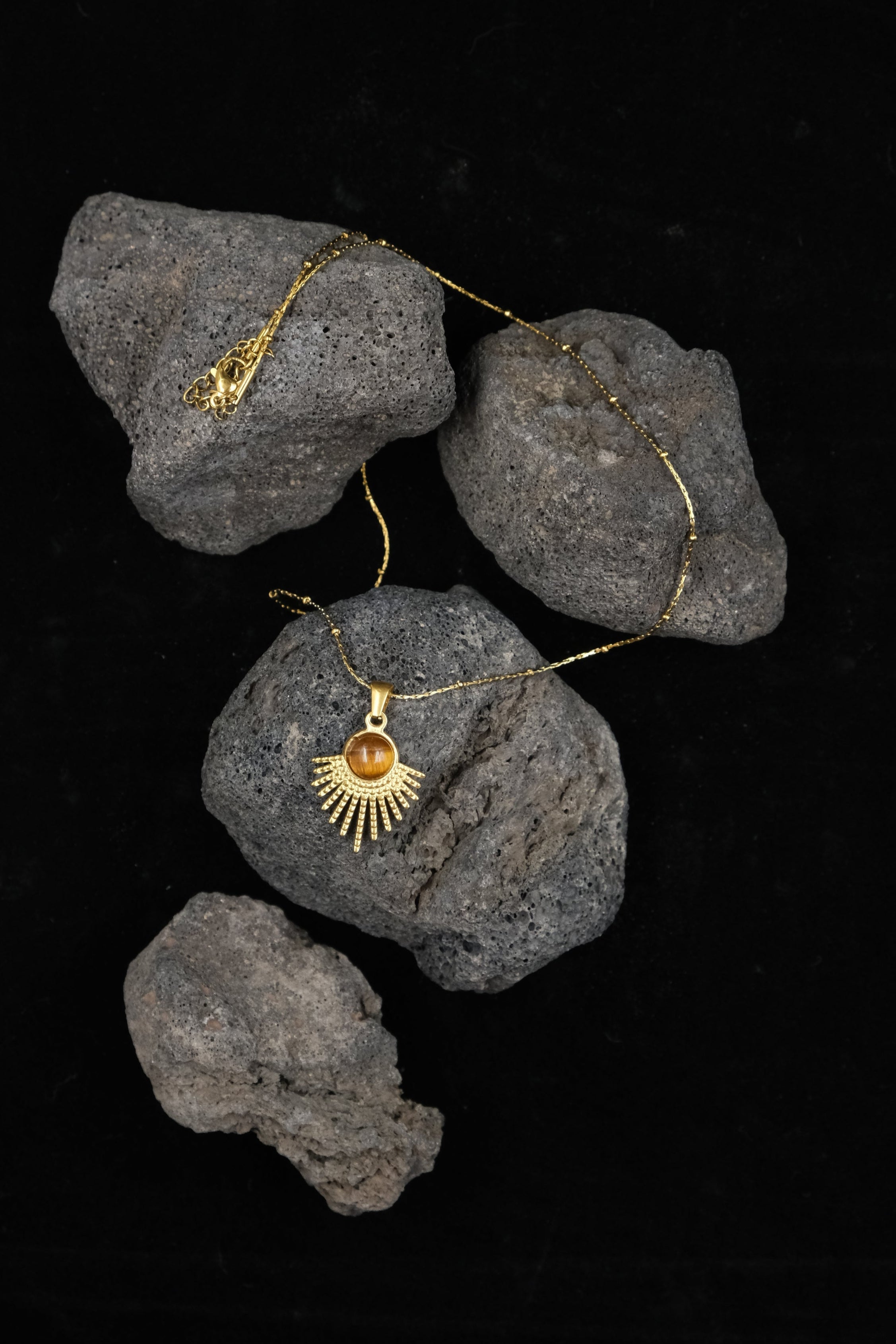 Tibetan Radiance Pendant Necklace with a sun design on tiger`s eye rocks against a black background