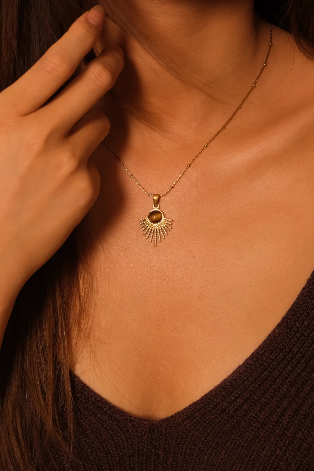 Close-up of a person wearing a Tibetan Radiance Pendant Necklacewith a pendant, hand touching the neck. Tiger’s Eye Sun for Success & Abundance