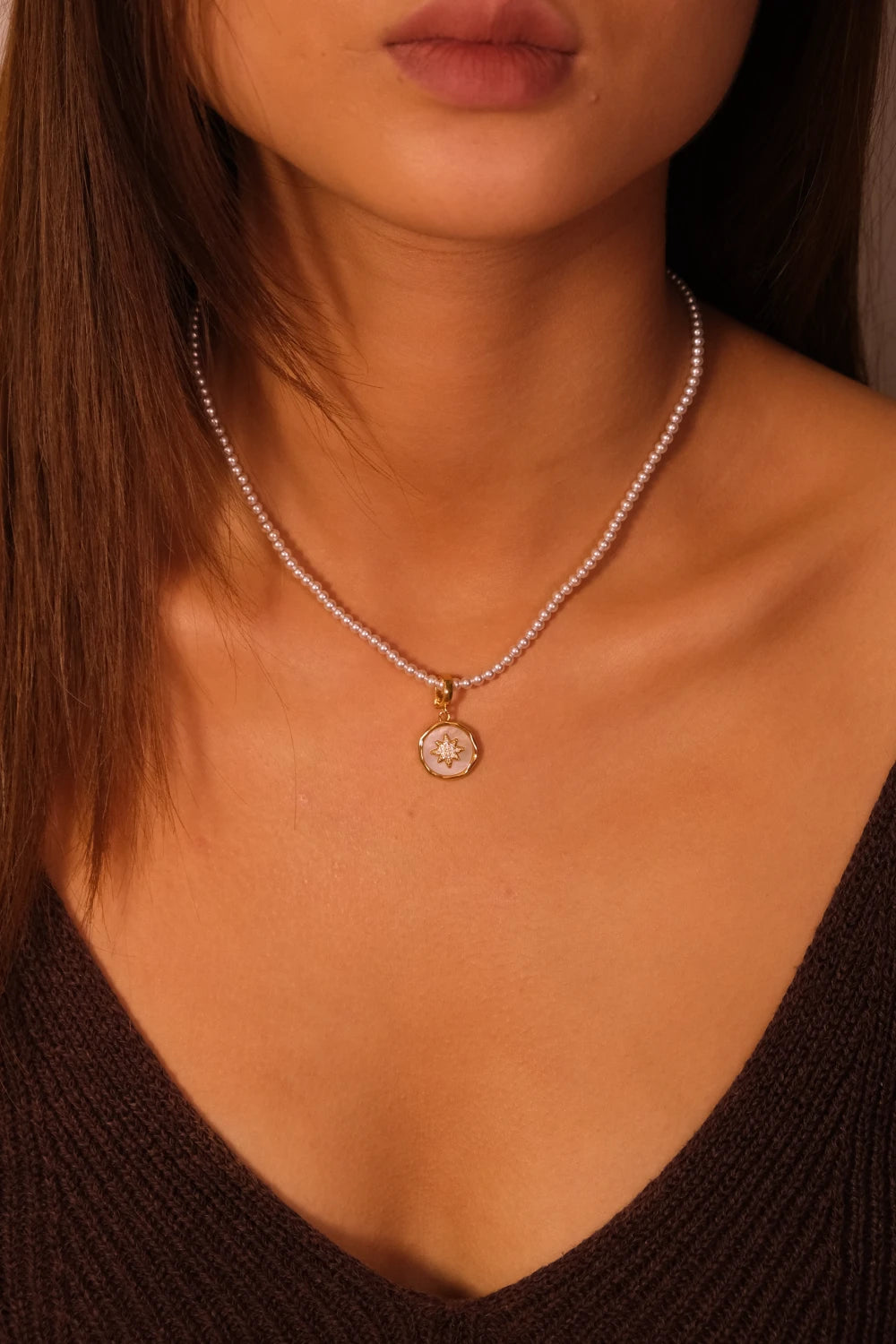 Close-up of a necklace with a pendant on a person wearing a brown top.