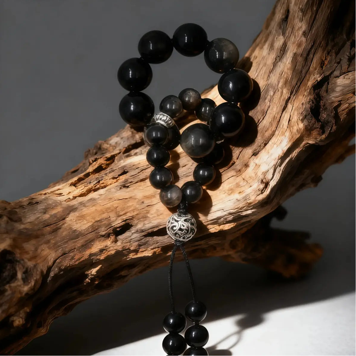 A strand of Black Obsidian and Silver Sheen Obsidian beads hanging from a rustic wooden branch.