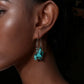 Close-up of a woman's ear wearing turquoise earrings with a dark background