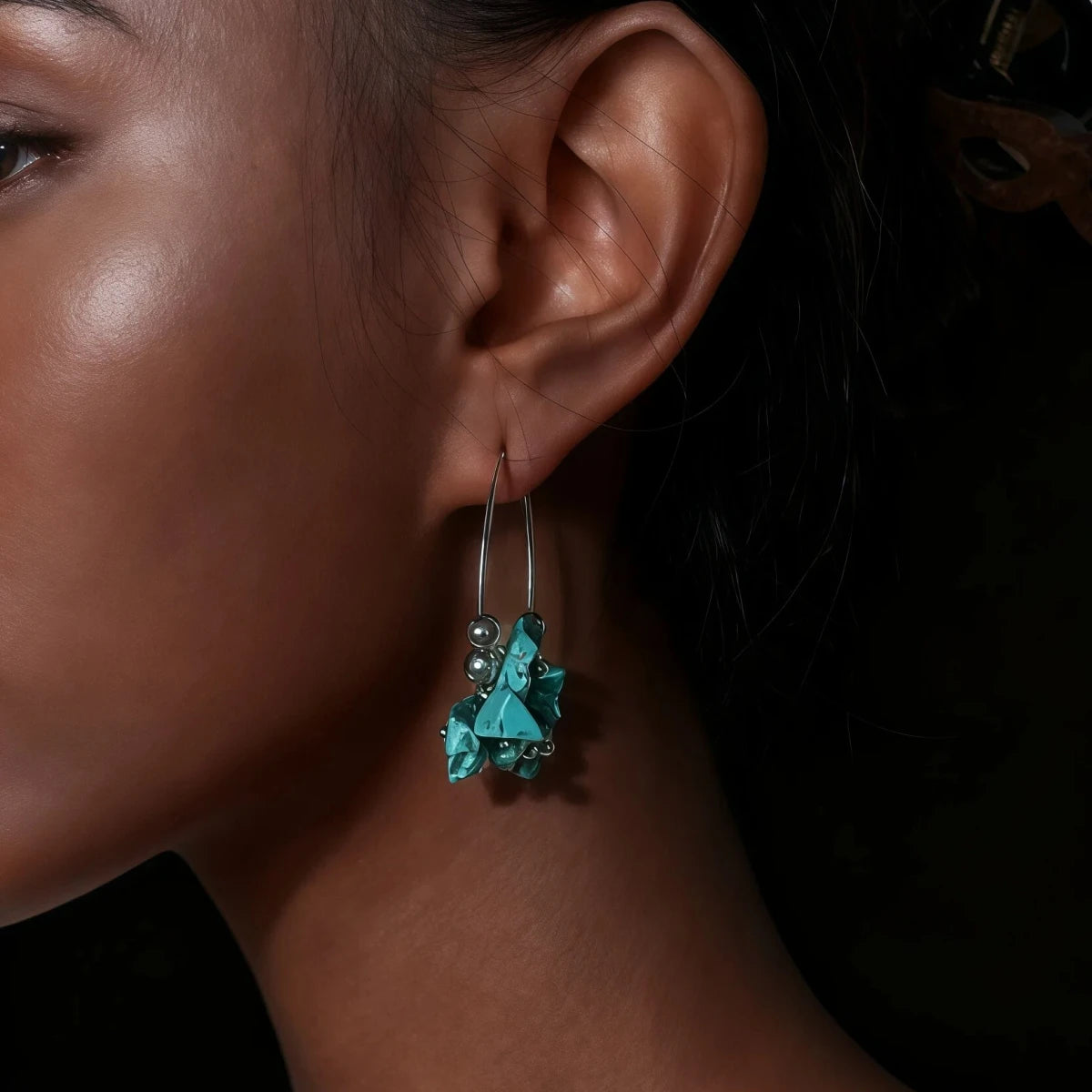 Close-up of a woman's ear wearing turquoise earrings with a dark background